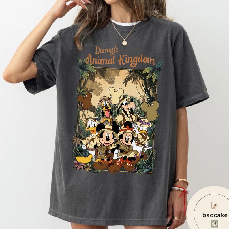 May include: Dark gray t-shirt featuring the text "Disney's Animal Kingdom" above a graphic of Disney characters in safari outfits. The graphic includes Mickey and Minnie Mouse, Donald Duck, Goofy, and Pluto.