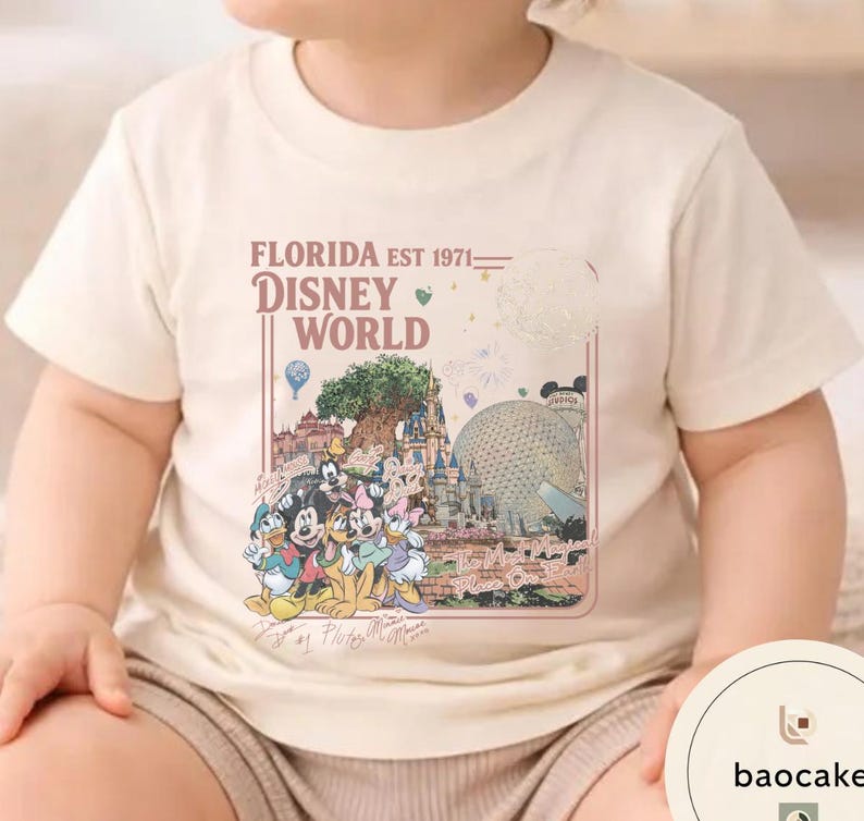 May include: A cream-colored short-sleeve t-shirt featuring a graphic print of Disney World landmarks and characters. The text reads Florida Est 1971 Disney World The Most Magical Place On Earth, with signatures of Mickey, Minnie, Donald, Goofy, and Pluto.
