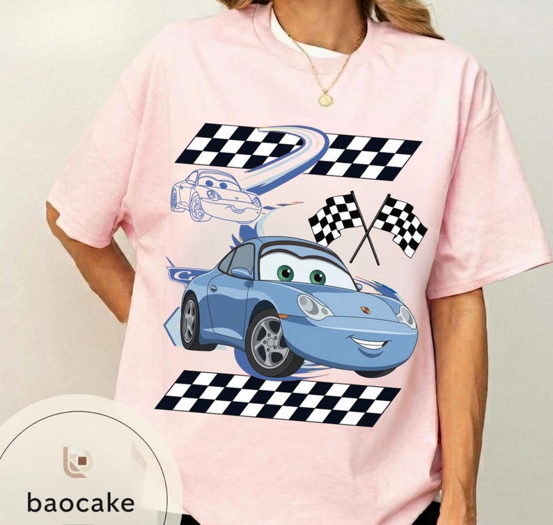 May include: A light pink t-shirt featuring a cartoon car design. The design includes a blue car with green eyes, checkered flags, and a checkered racing track. The text "baocake" is at the bottom.