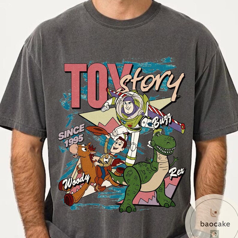 May include: Dark gray t-shirt featuring a graphic of Toy Story characters, including Buzz Lightyear, Woody, and Rex. The text "TOY story" is in pink and white, with "SINCE 1995" below. A vintage-style design.