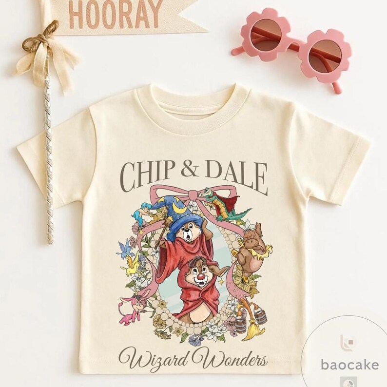 May include: Cream-colored t-shirt featuring the text "Chip & Dale" above a colorful graphic of the cartoon characters in wizard attire. The words "Wizard Wonders" are printed below the graphic. Pink flower-shaped sunglasses and a "Hooray" banner are also visible.
