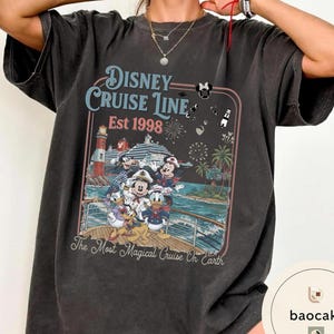 Puede incluir: Camiseta gris oscuro con un gr&aacute;fico colorido de personajes de Disney en un crucero. El dise&ntilde;o incluye el texto "Disney Cruise Line Est 1998" y "The Most Magical Cruise On Earth". La camiseta tiene un aspecto vintage.
