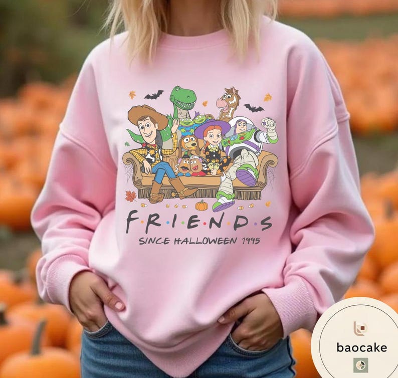 May include: A light pink long-sleeve sweatshirt featuring a graphic print of Toy Story characters sitting on a couch with the text "FRIENDS SINCE HALLOWEEN 1995". The design includes Woody, Buzz Lightyear, Jessie, Rex, Bullseye, and Slinky Dog.