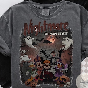 May include: Dark gray t-shirt with a Halloween-themed graphic. The design features the text "Nightmare on Main Street" above a spooky illustration of cartoon characters, ghosts, pumpkins, and a full moon. The shirt is made of a soft material.