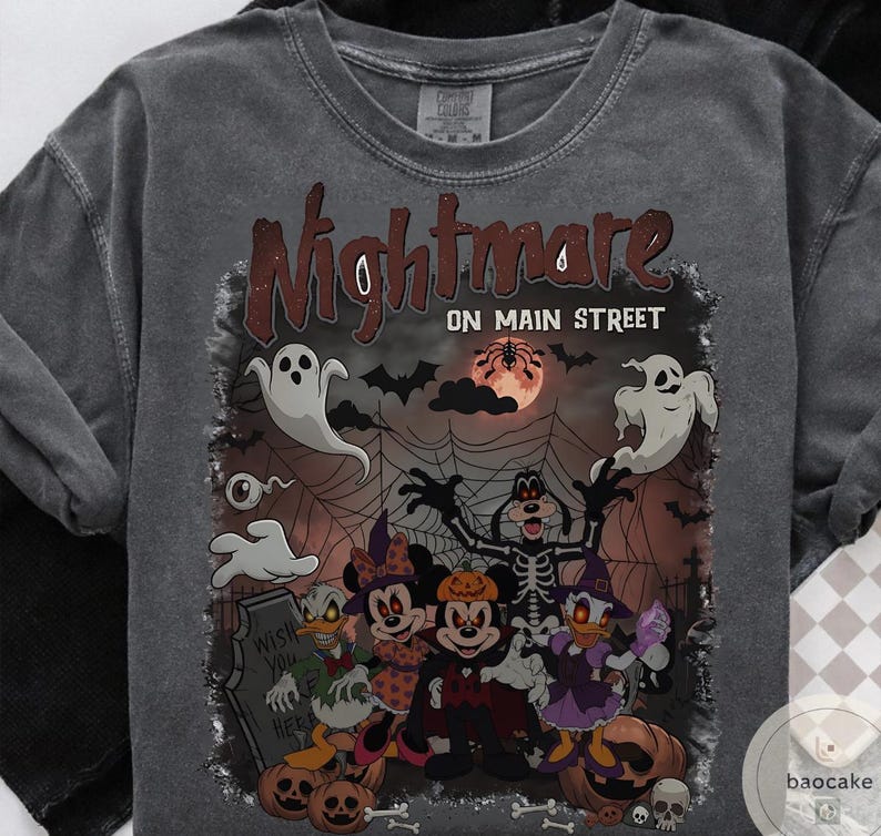 May include: Dark gray t-shirt with a Halloween-themed graphic. The design features the text "Nightmare on Main Street" above a spooky illustration of cartoon characters, ghosts, pumpkins, and a full moon. The shirt is made of a soft material.