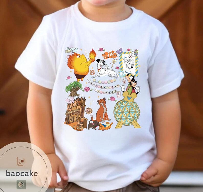 May include: White t-shirt featuring a colorful graphic with cartoon characters and the text "Happiest Day on Earth." The design includes a variety of animated figures, a tree, and a building. The shirt is worn by a child.