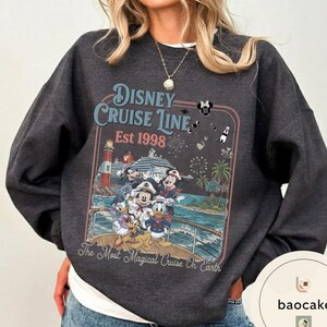 Puede incluir: Sudadera gris oscuro con un dise&ntilde;o de Disney Cruise Line. El gr&aacute;fico incluye a Mickey Mouse, el Pato Donald y otros personajes en un crucero, con el texto "Disney Cruise Line Est 1998" y "The Most Magical Cruise On Earth."