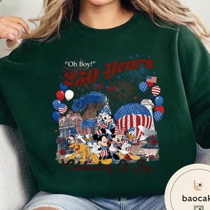 Puede incluir: Sudadera verde oscuro con un gr&aacute;fico colorido que celebra 250 a&ntilde;os. El dise&ntilde;o incluye fuegos artificiales, globos y personajes de Disney como Mickey y Minnie Mouse. El texto incluye "Oh Boy!" y "Celebrating of Joy."