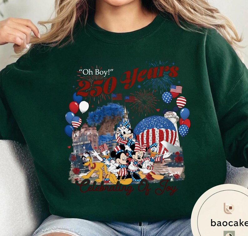 Puede incluir: Sudadera verde oscuro con un gr&aacute;fico colorido que celebra 250 a&ntilde;os. El dise&ntilde;o incluye fuegos artificiales, globos y personajes de Disney como Mickey y Minnie Mouse. El texto incluye "Oh Boy!" y "Celebrating of Joy."