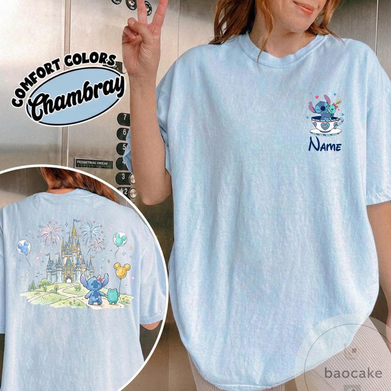May include: Light blue Comfort Colors Chambray t-shirt featuring a cartoon Stitch design. The front has a Stitch graphic in a teacup with the word "Name" below. The back shows Stitch in front of a castle with fireworks and balloons.