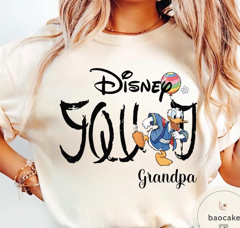 Puede incluir: Sudadera color crema con la inscripci&oacute;n "Disney Grandpa" en escritura negra, con una imagen de dibujos animados de Pato Donald sosteniendo un globo colorido. La palabra "Disney" est&aacute; arqueada sobre la palabra "Grandpa".