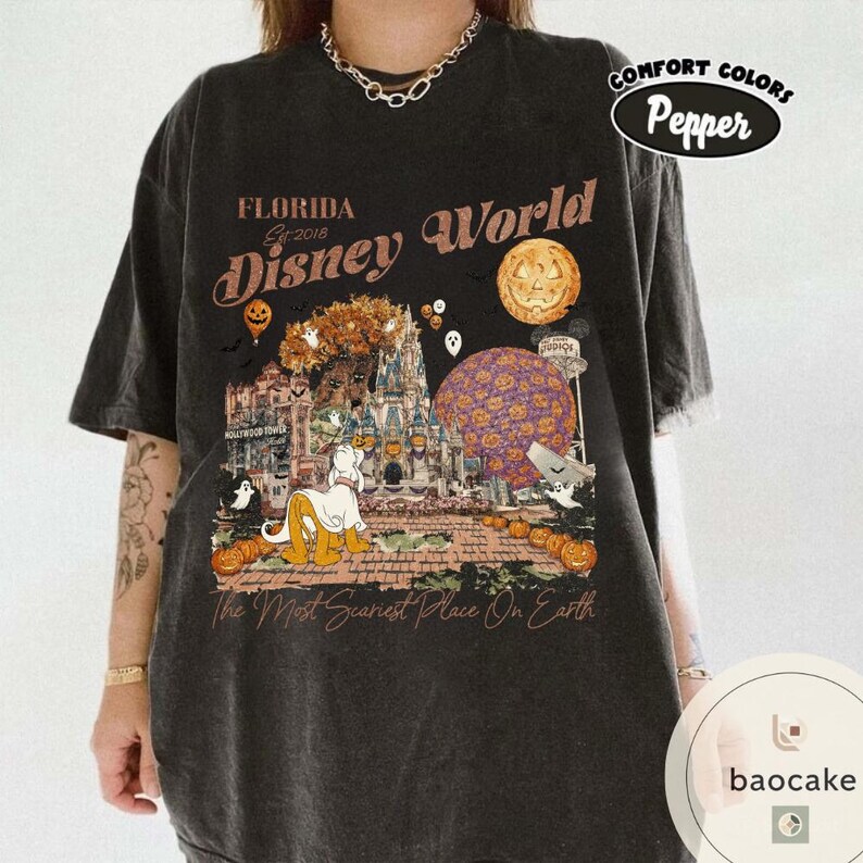 Op de afbeelding: Donkergrijs T-shirt met een Halloween-thema Disney World-afbeelding. Het ontwerp bevat pompoenen, geesten en een stripfiguur voor een kasteel. De tekst op het shirt luidt "Florida Disney World" en "The Most Scariest Place On Earth."