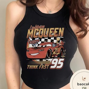 Puede incluir: Camiseta sin mangas negra con un gr&aacute;fico de Rayo McQueen de la pel&iacute;cula Cars. El dise&ntilde;o incluye el texto "Lightning McQueen", "Cars", "95" y "Think Fast". El coche es rojo con un fondo de cuadros.