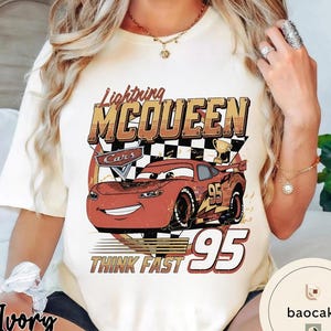 Puede incluir: Camiseta de color marfil con un gr&aacute;fico de Rayo McQueen de la pel&iacute;cula Cars. El dise&ntilde;o incluye el texto "Lightning McQueen", "Cars", "95" y "Think Fast". El coche de dibujos animados es rojo con detalles en negro y amarillo.