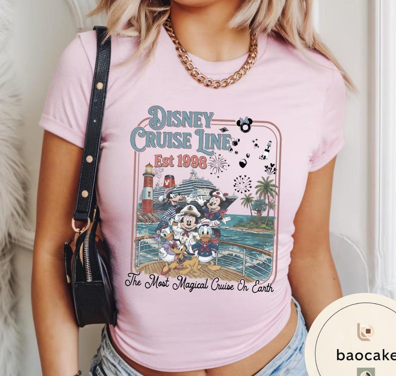 Puede incluir: Una camiseta rosa claro con un dise&ntilde;o de Disney Cruise Line. El dise&ntilde;o incluye a Mickey Mouse, Minnie Mouse, Donald Duck y otros personajes en un crucero, con el texto "Disney Cruise Line Est 1998" y "The Most Magical Cruise On Earth."