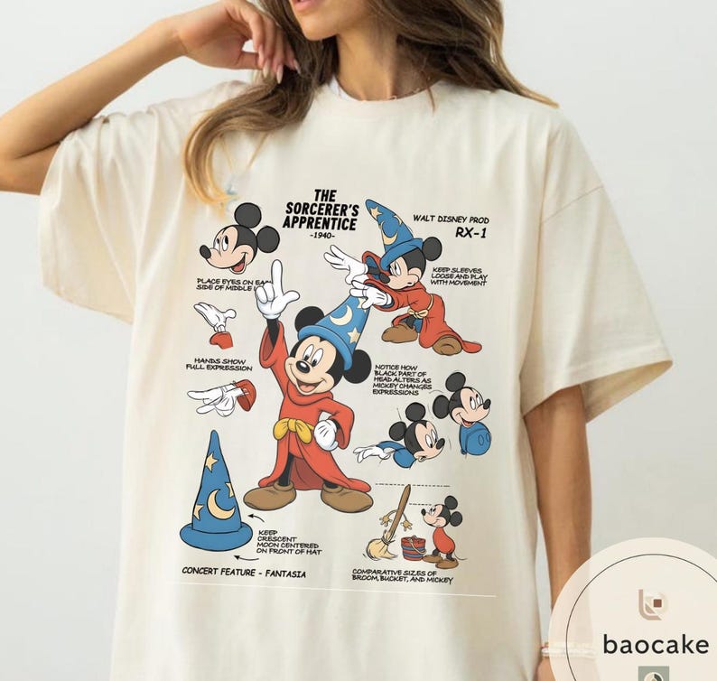 May include: Cream-colored t-shirt featuring a graphic of Mickey Mouse from "The Sorcerer's Apprentice" with text and illustrations. The design includes Mickey in a sorcerer's outfit, a blue hat, and various poses. The text includes "The Sorcerer's Apprentice -1940- Walt Disney Prod RX-1".