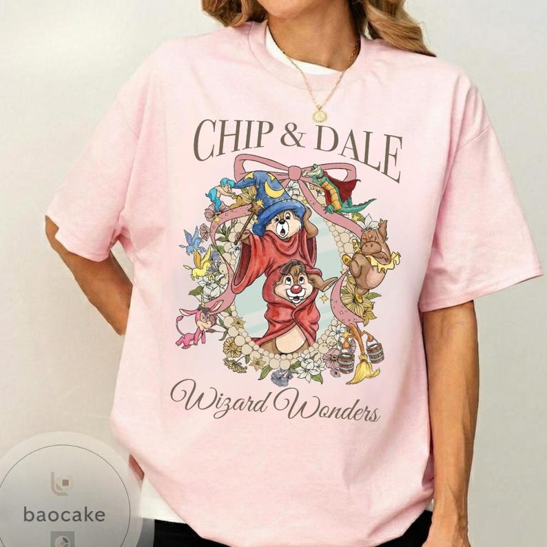 May include: A light pink t-shirt featuring the text "CHIP & DALE" above a colorful illustration of Chip and Dale in wizard attire, surrounded by a floral wreath. The words "Wizard Wonders" are printed below the illustration.