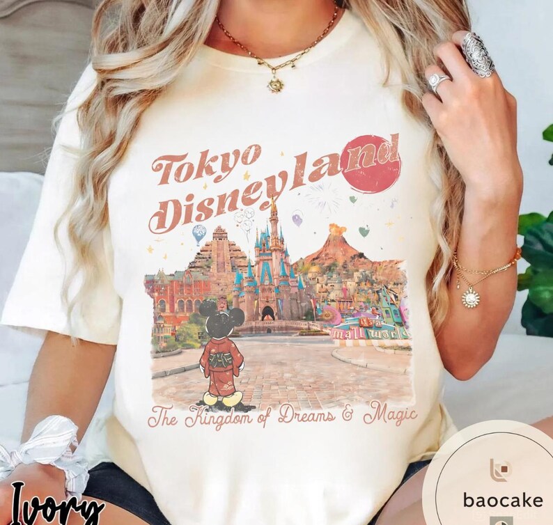 May include: Ivory-colored t-shirt featuring a graphic of Tokyo Disneyland with Mickey Mouse in a kimono. The text "Tokyo Disneyland" is in a retro font, and the phrase "The Kingdom of Dreams & Magic" is below the graphic.