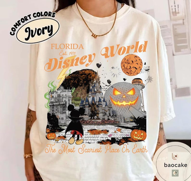 May include: Ivory-colored t-shirt featuring a Halloween-themed Disney World graphic. The design includes a pumpkin, Mickey Mouse in a cape, and the text "The Most Scariest Place On Earth." The shirt also has the words "Florida" and "Disney World."