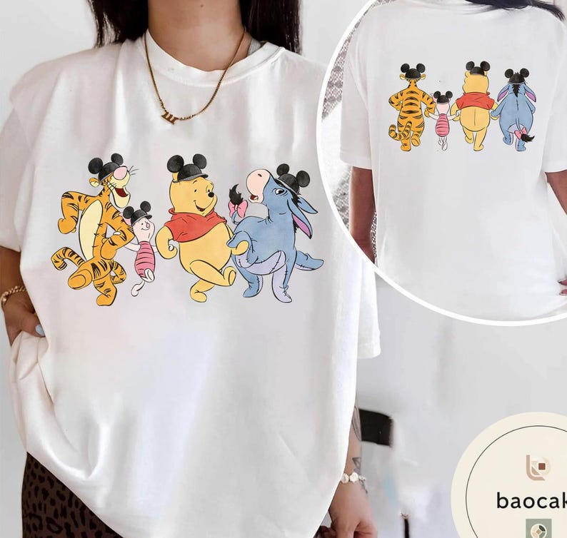 May include: White t-shirt featuring a colorful graphic of Winnie the Pooh characters: Tigger, Piglet, Winnie the Pooh, and Eeyore, all wearing Mickey Mouse ears. The back of the shirt also has the same characters. A fun, whimsical design.