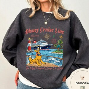 K&ouml;nnte beinhalten: Dunkelgraues Sweatshirt mit einem Disney Cruise Line-Motiv. Das Design zeigt ein Kreuzfahrtschiff, Pluto, einen Leuchtturm, Palmen und Feuerwerk. Der Text lautet "Disney Cruise Line Est. 1998" und "The Most Magical Cruise On Earth."