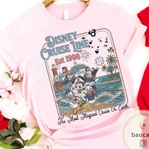 Puede incluir: Camiseta rosa claro con un dise&ntilde;o de personajes de Disney en un crucero. El dise&ntilde;o incluye el texto "Disney Cruise Line Est 1998" y "The Most Magical Cruise On Earth". La camiseta tiene mangas cortas.