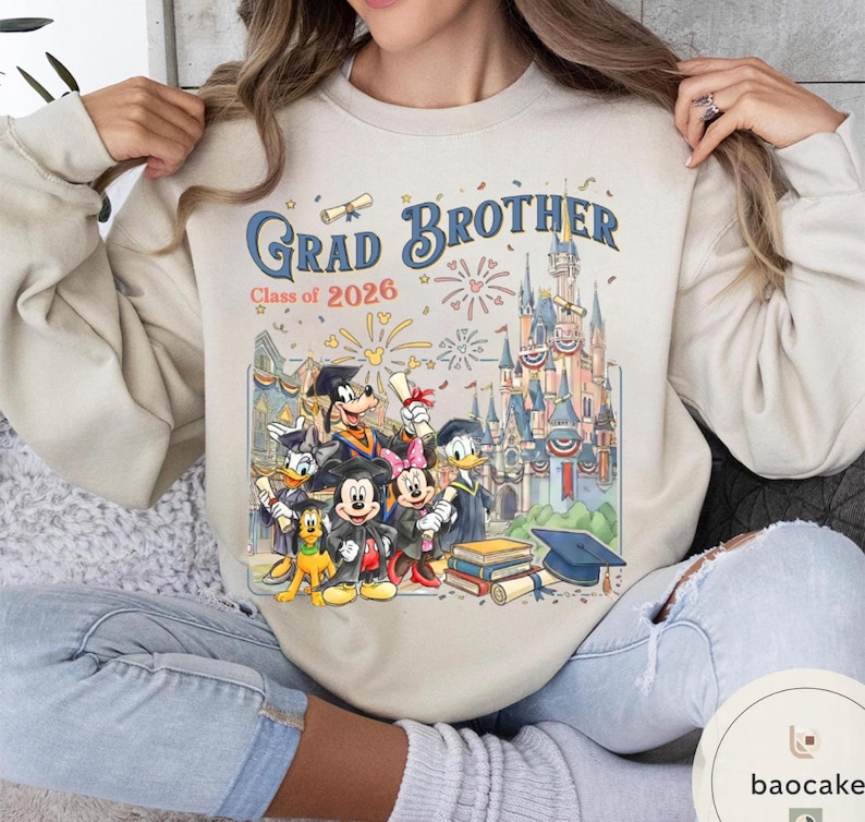 May include: Cream-coloured sweatshirt with a colourful graphic of Disney characters in graduation attire. The text "Grad Brother Class of 2026" is above an illustration of a castle and fireworks.