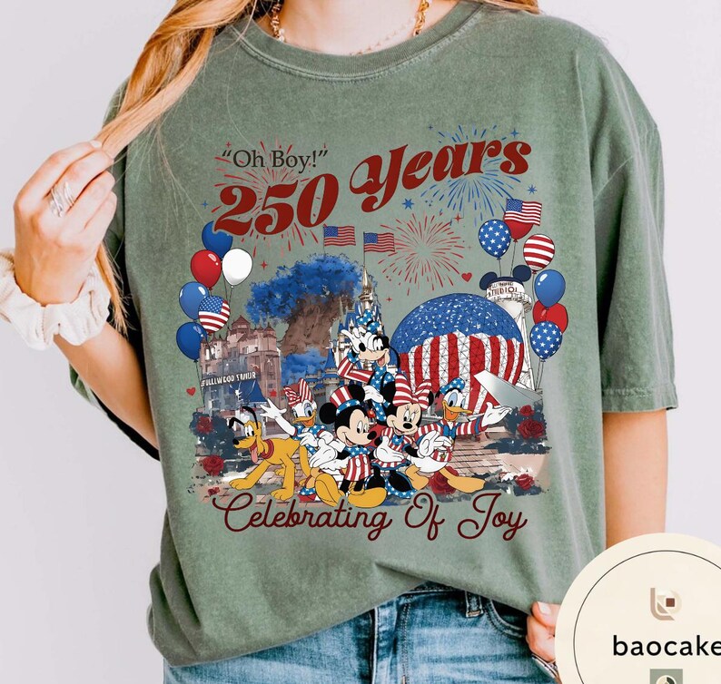Puede incluir: Camiseta verde salvia con un gr&aacute;fico que celebra 250 a&ntilde;os. El dise&ntilde;o incluye Mickey Mouse, Minnie Mouse, Donald Duck y Pluto, junto con fuegos artificiales, globos y banderas americanas. El texto incluye "Oh Boy!" y "Celebrating of Joy."