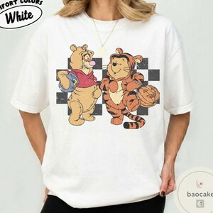 May include: White t-shirt with a distressed graphic featuring two cartoon characters, one dressed as a bear and the other as a tiger, standing in front of a black and white checkered pattern. The text "COMFORT COLORS White" is at the top.