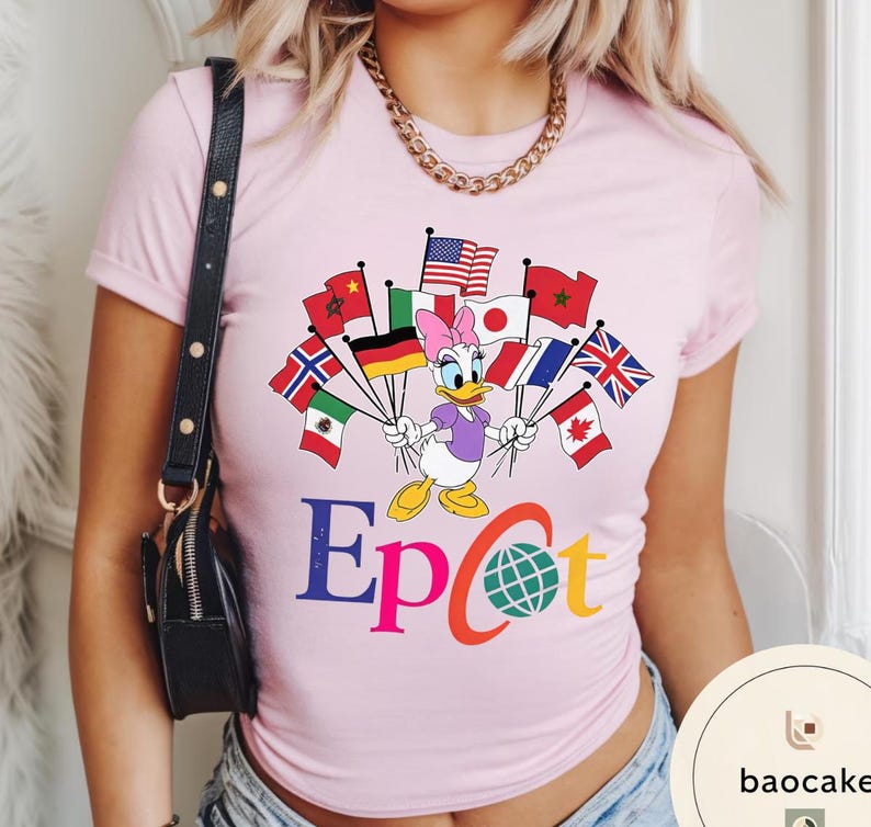 May include: A pale pink t-shirt with a Daisy Duck graphic holding flags from different nations. The word "Epcot" is printed in colourful letters below the character. A gold chain and black purse are also visible.