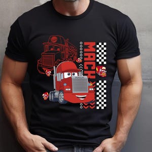 May include: Black t-shirt with a red cartoon truck design. The design includes the word "MACH" in red and white checkered patterns. The truck has a smiling face and the word "MACK".