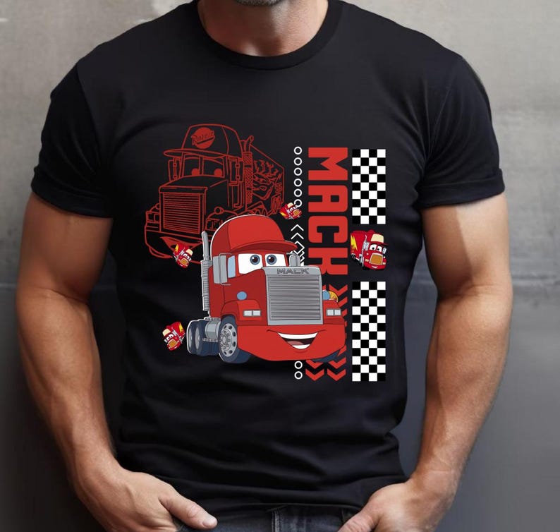 May include: Black t-shirt with a red cartoon truck design. The design includes the word "MACH" in red and white checkered patterns. The truck has a smiling face and the word "MACK".
