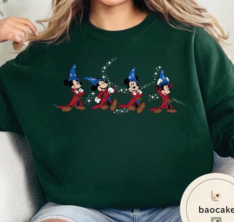 May include: Dark green sweatshirt featuring a graphic of Mickey Mouse in a wizard costume, with a blue hat and red robe. The design includes a starry trail. The sweatshirt is a solid color.