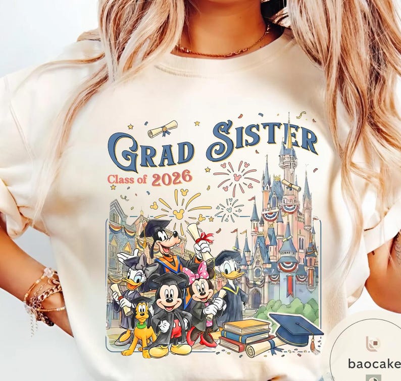 May include: Cream-coloured t-shirt with a colourful graphic. The design features the text "Grad Sister Class of 2026" and Disney characters in graduation attire, a castle, fireworks, and books. The graphic uses shades of blue, red, yellow, and black.