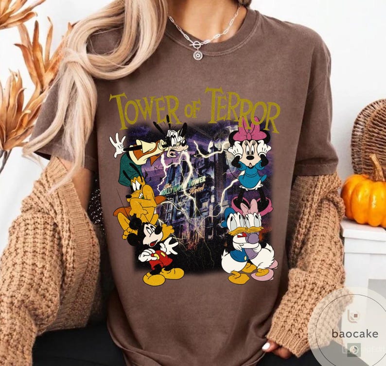 May include: Brown t-shirt featuring a graphic of Disney characters, including Mickey Mouse, Goofy, and Minnie Mouse, with the text "Tower of Terror." The design includes lightning and the Hollywood Tower Hotel.