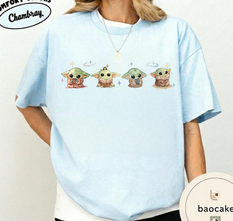May include: Light blue t-shirt featuring four cartoon characters in different outfits. The characters are green with large eyes and are surrounded by small stars. The shirt has the word "Chambray" printed on it.
