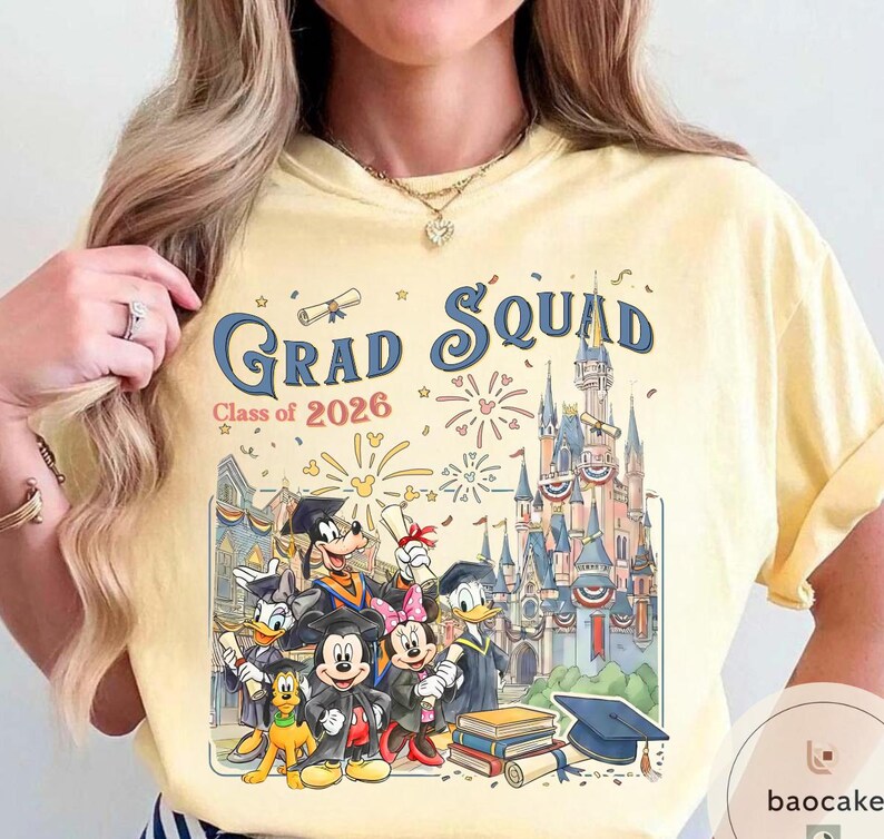 May include: A pale yellow t-shirt with a colourful graphic featuring Disney characters in graduation attire. The text "Grad Squad Class of 2026" is displayed above the characters and a castle.