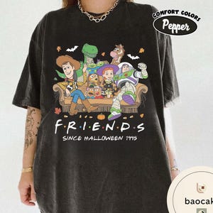 May include: A black short-sleeve t-shirt featuring a graphic of Toy Story characters sitting on a couch. The text reads F.R.I.E.N.D.S SINCE HALLOWEEN 1995. The design includes Woody, Buzz Lightyear, Jessie, Rex, Bullseye, and Mr. Potato Head with autumn leaves.