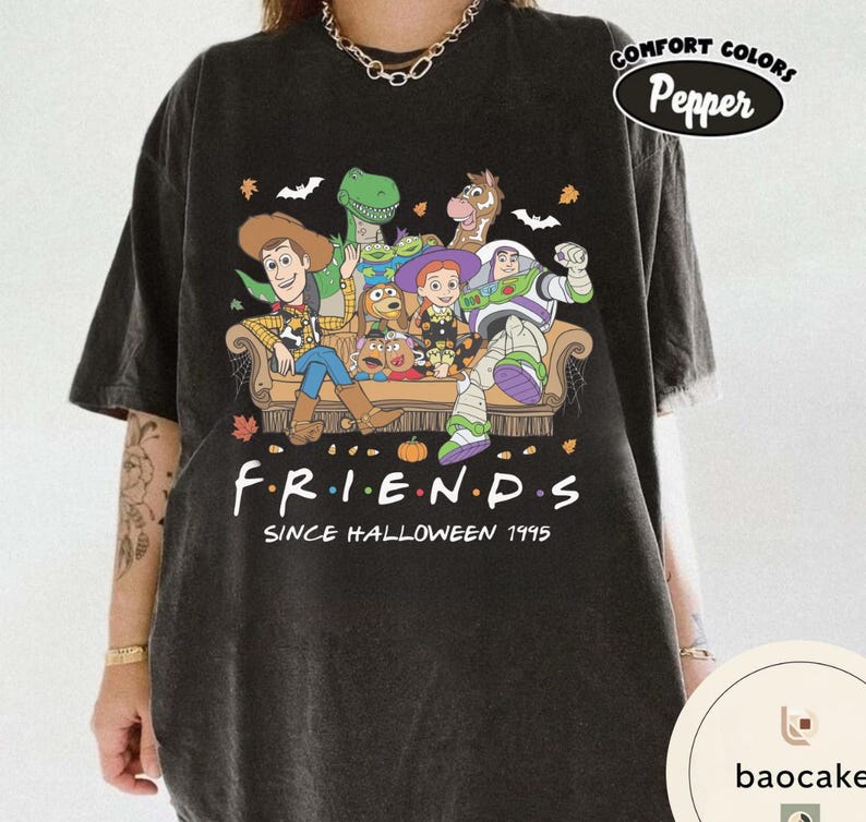 May include: A black short-sleeve t-shirt featuring a graphic of Toy Story characters sitting on a couch. The text reads F.R.I.E.N.D.S SINCE HALLOWEEN 1995. The design includes Woody, Buzz Lightyear, Jessie, Rex, Bullseye, and Mr. Potato Head with autumn leaves.