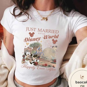 May include: White t-shirt with a graphic featuring Mickey and Minnie Mouse in wedding attire in front of a Disney World scene. The shirt has the text "Just Married Disney World Est 2026" and "Happily Ever After."