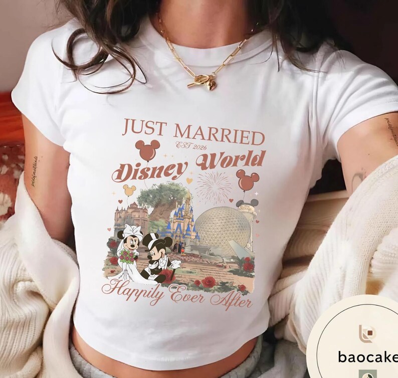 May include: White t-shirt with a graphic featuring Mickey and Minnie Mouse in wedding attire in front of a Disney World scene. The shirt has the text "Just Married Disney World Est 2026" and "Happily Ever After."