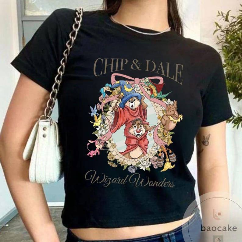 May include: Black t-shirt featuring Chip and Dale in wizard attire, surrounded by a floral wreath. The text "Chip & Dale" arches across the top, with "Wizard Wonders" below. The design includes a blue wizard hat and red robes.