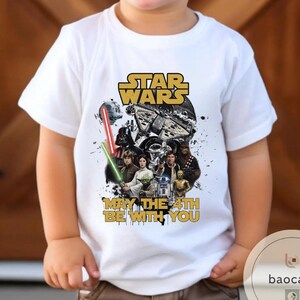 Puede incluir: Camiseta blanca con un dise&ntilde;o de Star Wars. El dise&ntilde;o incluye el logotipo de Star Wars, personajes y la frase "May the 4th Be With You". El gr&aacute;fico tiene un aspecto vintage y desgastado.