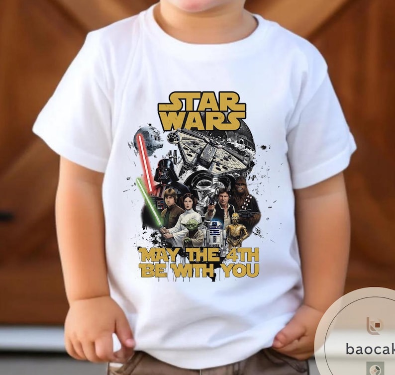 Puede incluir: Camiseta blanca con un dise&ntilde;o de Star Wars. El dise&ntilde;o incluye el logotipo de Star Wars, personajes y la frase "May the 4th Be With You". El gr&aacute;fico tiene un aspecto vintage y desgastado.