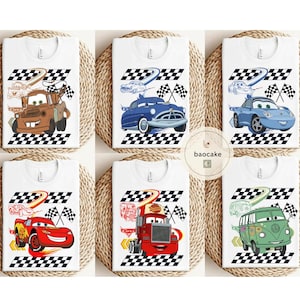 May include: White t-shirts featuring cartoon car designs. Each shirt showcases a different car character with a checkered flag and racing track graphic. The designs include a brown tow truck, a blue classic car, and a red race car.