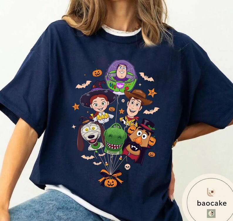 Pode incluir: Uma t-shirt azul-marinho com uma estampa gr&aacute;fica de v&aacute;rios personagens animados vestidos com fantasias de Halloween, incluindo um patrulheiro espacial, uma cowgirl, um cowboy, um dinossauro, um c&atilde;o e uma batata, presos a um bal&atilde;o de ab&oacute;bora.