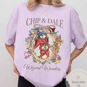 May include: A light purple t-shirt featuring Chip and Dale in a wizard-themed design. The graphic includes the text "Chip & Dale" above a circular floral frame with the words "Wizard Wonders" below. The design is in a cartoon style.
