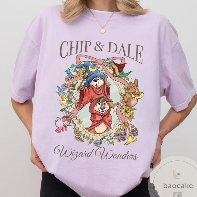 May include: A light purple t-shirt featuring Chip and Dale in a wizard-themed design. The graphic includes the text "Chip & Dale" above a circular floral frame with the words "Wizard Wonders" below. The design is in a cartoon style.