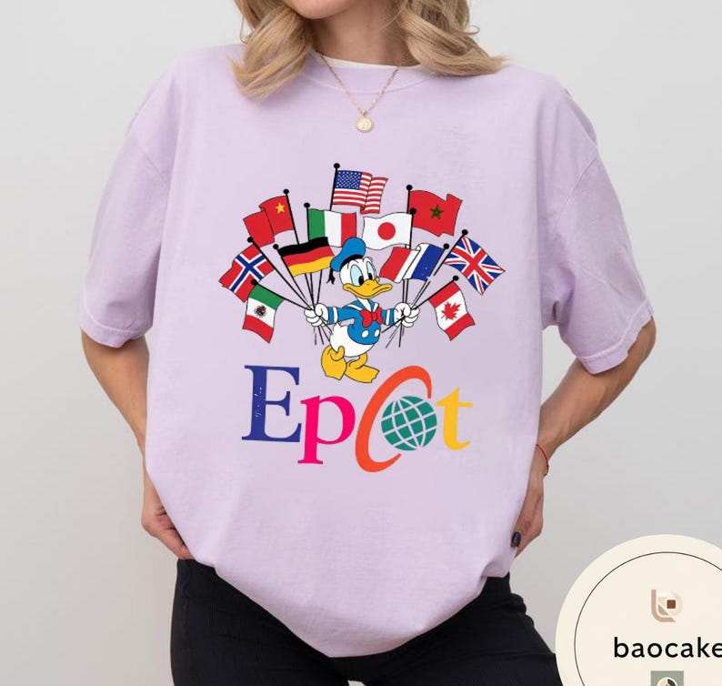 May include: A lilac t-shirt with a graphic of Donald Duck holding flags from different nations. The word "Epcot" is written in colourful letters below the character, with a globe graphic in the letter "C".