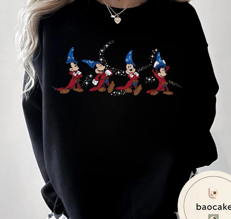 May include: Black sweatshirt featuring a cartoon graphic of Mickey Mouse in a sorcerer's outfit. The design shows Mickey in a red robe and blue wizard hat, with a trail of sparkling stars. The sweatshirt is a casual style.